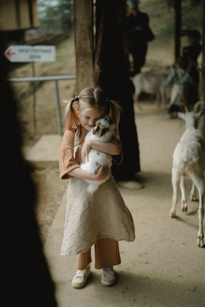 A young girl lovingly hugs a small goat on a rural farm pathway, showcasing childhood innocence.