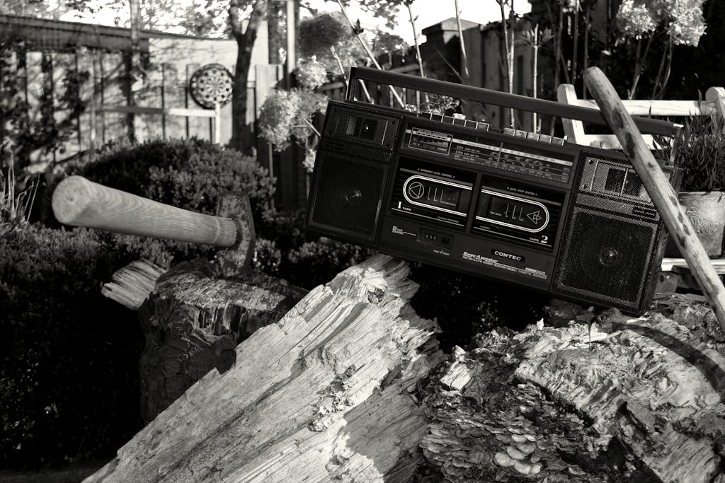 Retro boombox perched on a log with an axe in a rustic garden setting.