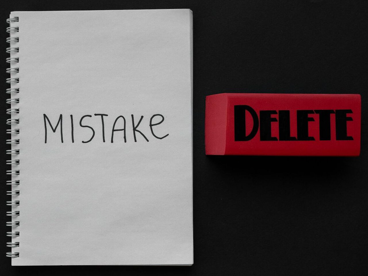 Flat lay of a notebook with 'Mistake' and red eraser labeled 'Delete', minimalist concept.