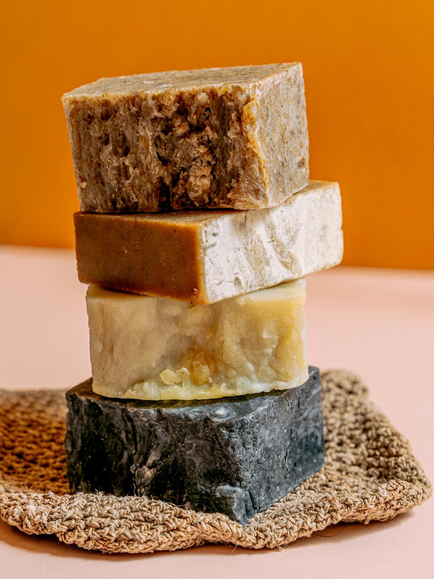 Four handmade natural soap bars stacked on a textured mat against a warm background.