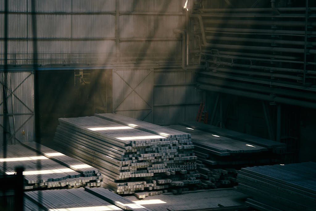 Sunlight streams into an industrial warehouse illuminating stacked steel beams.