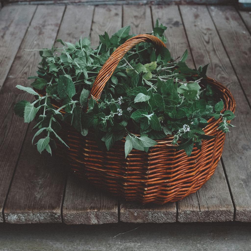 A woven basket filled with fresh green herbs on a wooden table, showcasing a rustic scene.
